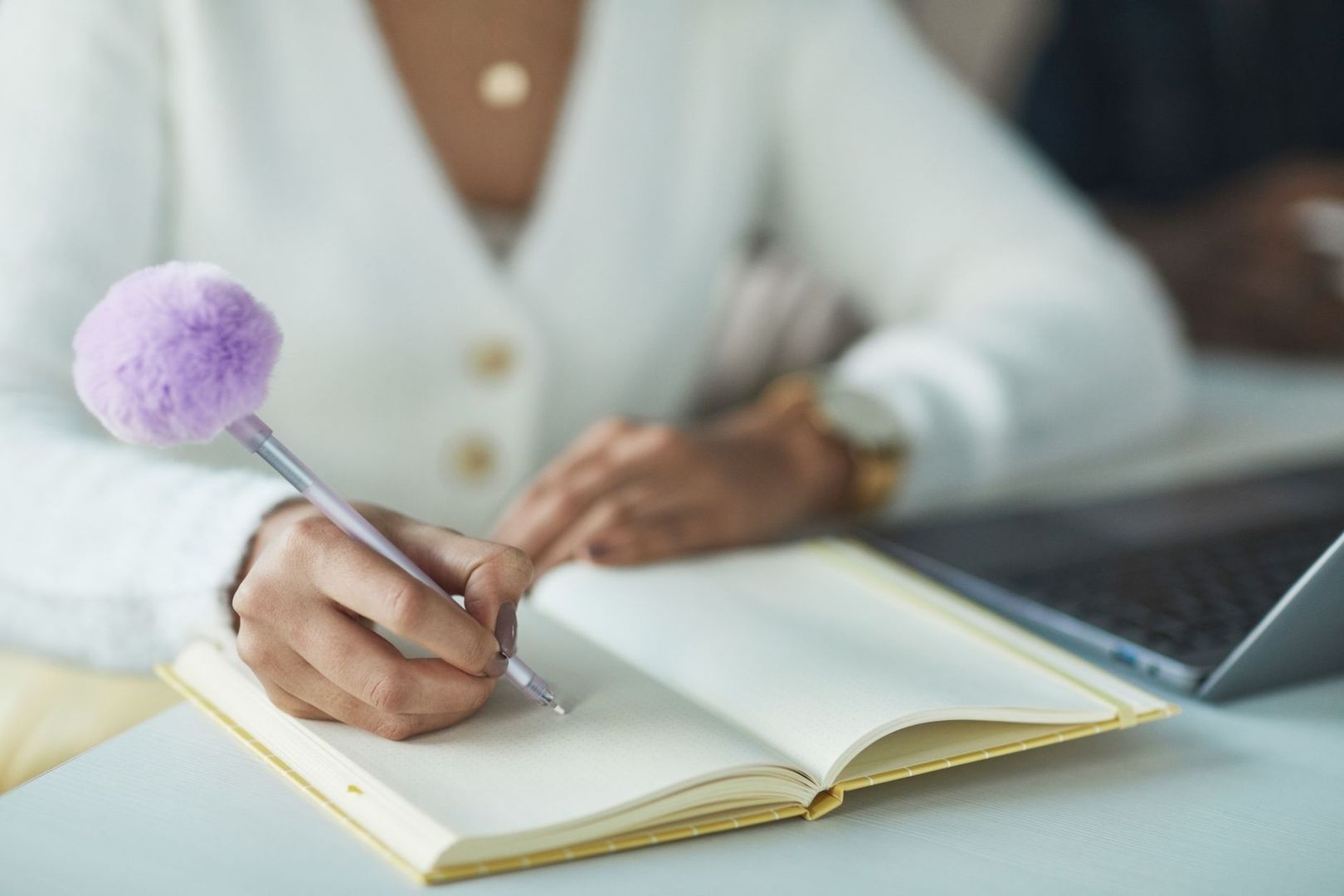 Person schreibt mit einem fliederfarbenen Stift in ein offenes Notizbuch